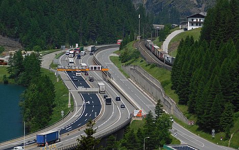 image showing the Brenner Highway and the Brenner railway side by side at Venntal, close to Brenner lake and the highest point of Brenner pass. There are cars and trucks on the Brenner Highway and a freight train on the Brenner railway